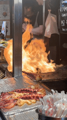Food stall workers prepare flaming dish in Jeju