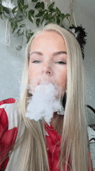 Woman smoking indoors near white wall with plants