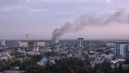 Black smoke billows over a city skyline at dusk