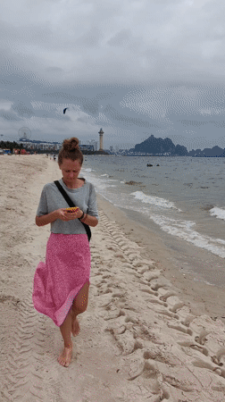 Woman walks barefoot on Vietnamese beach under overcast morning sky