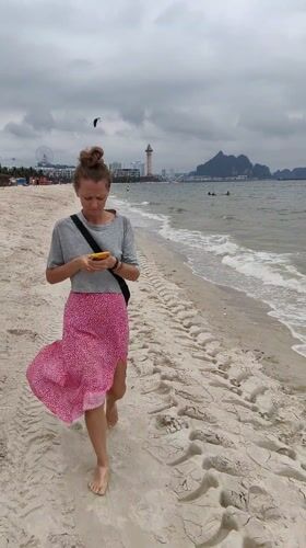Woman walks barefoot on Vietnamese beach under overcast morning sky