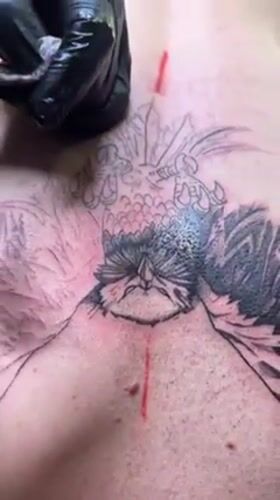 Tattoo artist creates large bird design on client's back