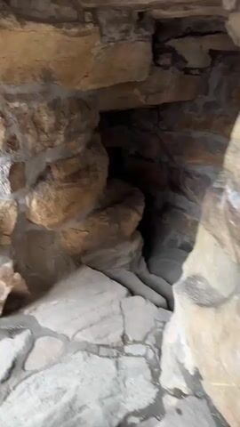 The video displays a close-up, panning view inside a structure built with rocks and mortar. The walls are composed of irregular, light brown and grey stones of varying sizes, connected by visible mortar lines. The camera slowly pans to the right, revealing the rough, textured surface of the rock interior and a darker, recessed area further into the structure. No individuals or other objects are visible.
