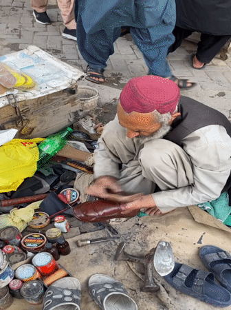 Elderly shoemaker works in busy Quetta market amid local commerce