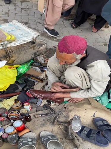 Elderly shoemaker works in busy Quetta market amid local commerce