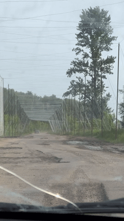 Vehicle travels damaged road with metal barriers in Derhachi
