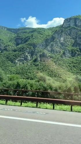 Mountain road driving through green alpine terrain in Nomi, Italy