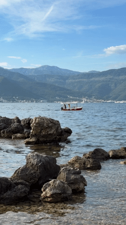 Red boat sails Montenegro coast amid mountain scenery