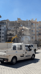 Excavator demolishes partially collapsed building in urban area