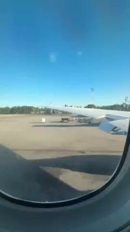 The video shows the wing of an airplane from an inside window. The plane is sitting on the tarmac. It's a clear day.