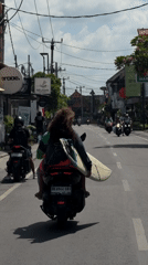 Scooters moving through North Kuta, one carrying a surfboard