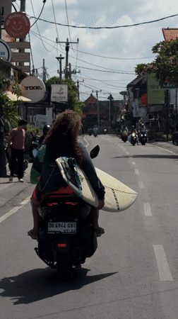 Scooters moving through North Kuta, one carrying a surfboard
