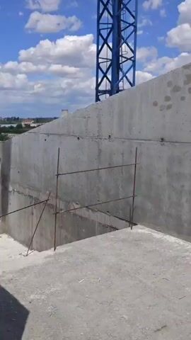 The video shows a construction crane against a blue sky with white clouds. The crane is blue and consists of a vertical tower and a long horizontal boom. At the end of the boom, there is a counterweight. There is a small cabin on the vertical tower. The camera angle is from below, looking up at the crane. The video appears to be a short, static shot.