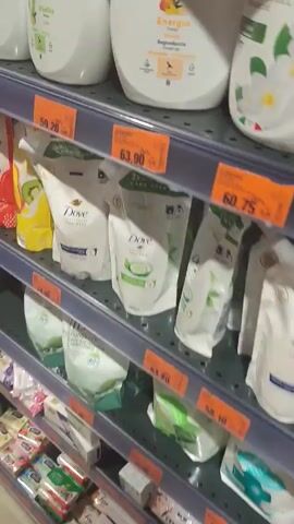 This short video showcases a retail environment, likely a supermarket or pharmacy, featuring rows of personal care products on shelves. The primary focus is on bottles of shower gel and hand soap.

**Objects:** Several large, white, opaque bottles of shower gel are prominently displayed on the top shelf. One bottle, labeled "DERMO med" with "Energia" and "Mango" text, is clearly visible, along with illustrations of mango slices and what appear to be peach slices. Another bottle to its left has green labeling. On the shelf below, there are multiple white pouches of Dove hand soap or body wash, some featuring green accents and illustrations of limes. Price tags are visible on the shelves, indicating sales and discounts.

**Scene and Setting:** The setting is a well-lit retail store, evident from the shelving units and the array of products. The lighting suggests it could be daytime, or the store is brightly illuminated. The presence of various consumer goods points to a commercial space. The location context provided is Vulcănești, Moldova.

**Activity:** The video appears to be a product showcase or perhaps someone browsing the aisles of the store. The camera pans across the shelves, highlighting different products.

**Notable Details:**
*   **Text:** Visible text includes brand names like "DERMO med," "Dove," and product line names like "Energia," "Mango," "Bagnodoccia," "Shower gel," "Idratante," "Hydrating," "Vitalità," and "Lime." Price tags display prices such as "59.20," "63.90," and "79.90," along with discount percentages like "-20%". Some labels mention "NEW" and "my moment."
*   **Visual Cues:** The color scheme of the products varies, with white bottles and packaging dominating, accented by colors like orange (from the mango illustration) and green (from lime illustrations and other product labels).

The overall impression is a typical retail display of personal hygiene products in a Moldovan store.