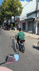 Scooter rider transports bicycle on handlebars in Vietnam
