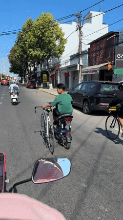Scooter rider transports bicycle on handlebars in Vietnam