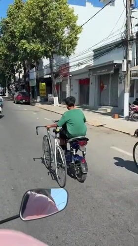 Scooter rider transports bicycle on handlebars in Vietnam