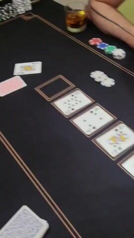 A hand of poker is being played on a black felt table with gold trim. There are several piles of poker chips in various colors, a drink with ice and a garnish in a glass, and several playing cards laid out. One player's hand is visible, holding a stack of cards. The community cards on the table are a 2 of diamonds, a Queen of hearts, a 4 of spades, a 10 of spades, and an empty spot. There are also two individual cards face up on the table: a King of diamonds and a 2 of spades. The video shows a close-up of the table from a slightly elevated angle, focusing on the cards and chips.