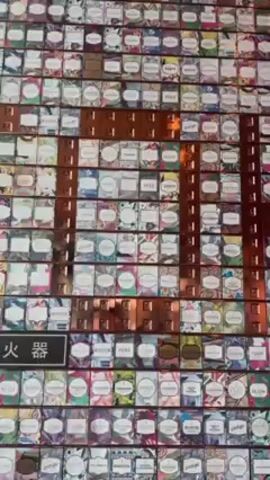 The video shows a wall covered in small boxes. Each box has a colorful floral background and a label. The boxes are arranged in rows and columns, with narrow metal strips separating the rows. Some boxes have place names written on their labels, such as "Peru," "Colombia," and "Indonesia." The camera pans across the wall, showing the extent of the collection. Two people are speaking in the background.