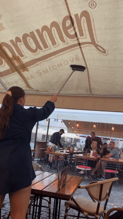 Prague restaurant worker clears water from dining patio awning