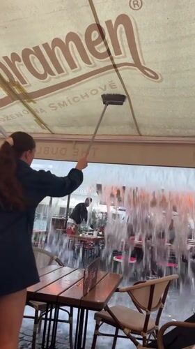 Prague restaurant worker clears water from dining patio awning
