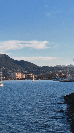 Sailboats navigate waters near Dénia harbor lighthouse, Spain