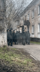 Military-uniformed group walks past damaged building in Perm