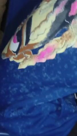 The video shows a close-up of a person's arm with a blue fabric, possibly a shirt or jacket, that has a colorful, abstract design on it. The design features wavy lines in shades of yellow, brown, black, and pink against a dark background. The blue fabric itself has a speckled pattern. The camera then pans to show the person holding a smartphone. The person's face is partially visible, and they appear to be looking down at the phone. The setting seems to be indoors, given the lighting. There is no visible text in the video. The overall impression is a casual moment of someone using their phone.