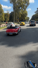 Motorcycle follows classic convertible on sunny Buenos Aires street