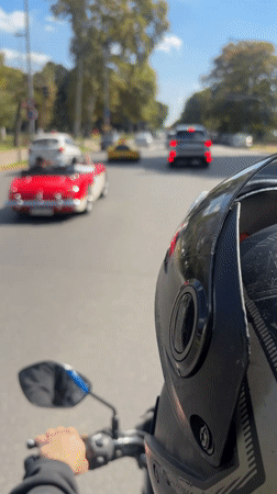 Motorcycle follows classic convertible on sunny Buenos Aires street