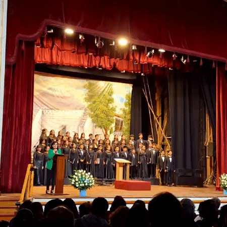Woman addresses audience with youth choir on Arequipa stage