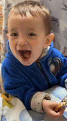 Toddler enjoys chocolate snack indoors wearing blue jacket