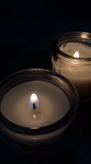 Two lit candles in glass jars observed in darkness