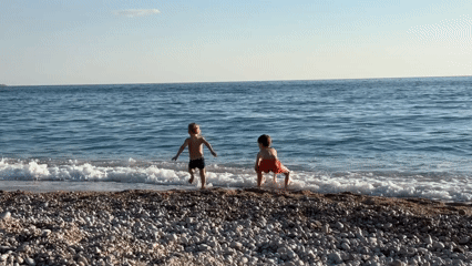 Children play on Fethiye beach as sailboat passes offshore