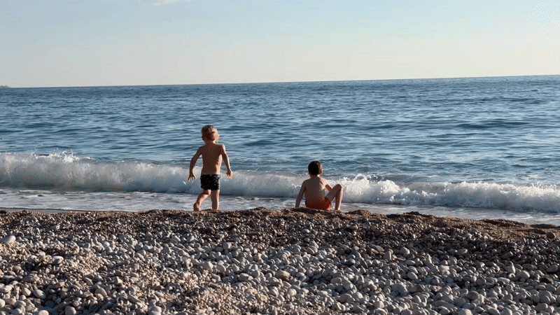Children play on Fethiye beach as sailboat passes offshore