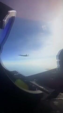 The video shows a first-person view from the cockpit of an aircraft. Above and in front of the camera, a larger aircraft is visible, its tail and engines clearly seen against a blue sky. A refueling boom extends from the larger aircraft downwards towards the camera's aircraft. The refueling boom is attached to the larger aircraft and appears to be in the process of refueling or preparing to refuel the camera's aircraft. The scene takes place at high altitude, with clouds or haze visible on the horizon. The larger aircraft has markings on its tail that read "6 ARW" and "427 ARW". The refueling boom has an orange glow at its tip.
