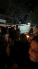 Nighttime candlelight gathering documented near building with trees