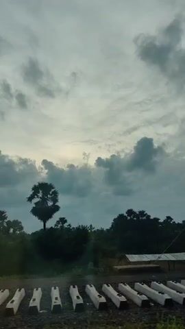 The video shows a series of railroad ties laid out in a row, with a cloudy sky overhead. The camera pans across the scene, revealing a utility pole with wires and trees in the background. A small structure, possibly a shed or shelter, is visible among the trees. The overall impression is of a rural or industrial area under a gray sky.