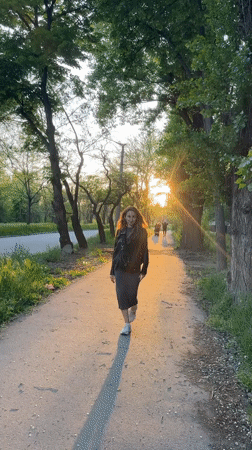 Woman walks tree-lined pathway in evening light, Kryvyi Rih