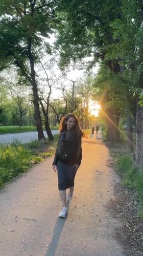 Woman walks tree-lined pathway in evening light, Kryvyi Rih