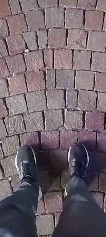 The video starts with a close-up shot of a person's feet in black sneakers standing on a cobblestone surface. The camera moves upward, revealing a white obelisk lit up against the night sky. There are a few people standing near the base of the obelisk. The camera pans up to show the full height of the obelisk, which has some text inscribed on its lower part. The rest of the frame is filled with the dark night sky.
