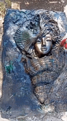 Metallic face sculpture gets painted outdoors, detail work in progress