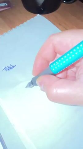 The video shows a close-up of a hand holding a teal and gray fountain pen with yellow dots. The hand is writing the word "Today" on a white notepad. The pen tip is visible as it moves across the paper, leaving a trail of dark blue ink. In the background, a portion of a wooden surface is visible, suggesting the notepad is on a table.