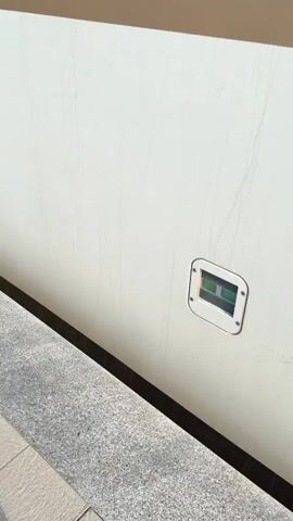 The video shows a train exterior. The first shot focuses on a closed train door, bronze in color with a small window near the top revealing some clothing inside. The next shot pans upwards to reveal the train's exterior color scheme of gray, gold, and white, with the word "STADLER" printed in bright blue. The final shot shows the train's front end, which is gray, white, and red. It has a number "ES2-009" displayed. The train is parked at a station platform.
