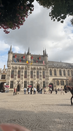 Horse-drawn carriages circle Bruges' Markt square on a summer afternoon