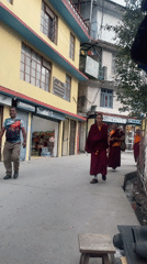 Buddhist monks walk streets while cobbler repairs sandals in Dharamkot