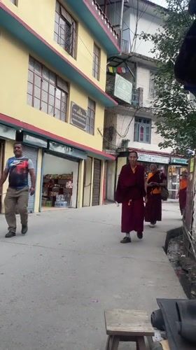 Buddhist monks walk streets while cobbler repairs sandals in Dharamkot