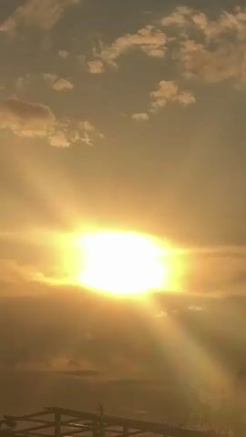 The video opens with a view of a bright sun behind clouds, with visible sun rays. The camera pans upward to reveal a blue sky with scattered white clouds.  The camera continues to pan up, showing a less cloudy portion of the sky before stopping.