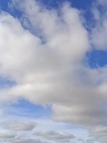 The video shows a sky with white clouds and blue patches. The clouds vary in size and shape, some appearing dense and others wispy. The blue sky is visible between and around the clouds. The video appears to be shot from a stationary position, capturing the movement of the clouds.