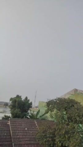 THE VIDEO SHOWS AN OVERCAST SKY ABOVE A FEW BUILDINGS AND TREES. A COMMUNICATIONS TOWER IS VISIBLE IN THE DISTANCE.